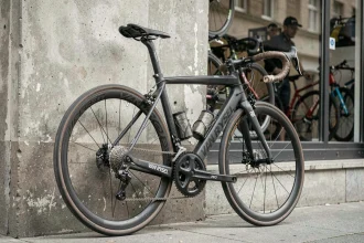 Vélo de route Van Rysel RCR Pro d'occasion appuyé contre un mur en béton usé, montrant des traces d'utilisation sur le cadre carbone mat